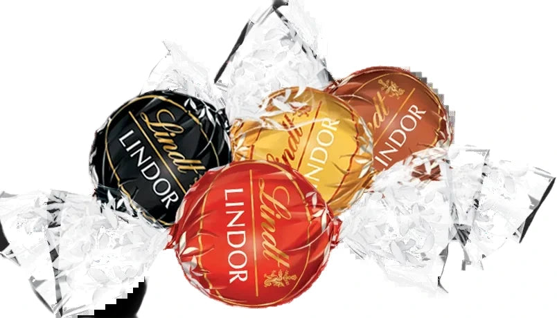 Four Lindtor Lindor chocolates in assorted foil wrappers, including black, gold, red, and brown, arranged on a white background with crumpled clear wrapping paper.