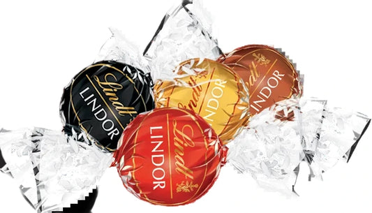 Four Lindtor Lindor chocolates in assorted foil wrappers, including black, gold, red, and brown, arranged on a white background with crumpled clear wrapping paper.