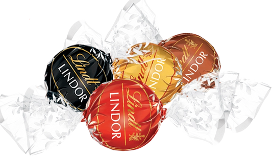 Four Lindtor Lindor chocolates in assorted foil wrappers, including black, gold, red, and brown, arranged on a white background with crumpled clear wrapping paper.